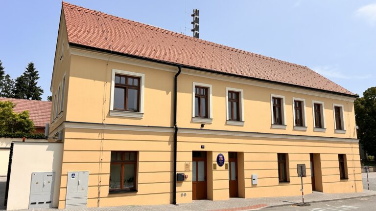 Žlutá fasáda dvoupodlažní budovy se sedlovou střechou