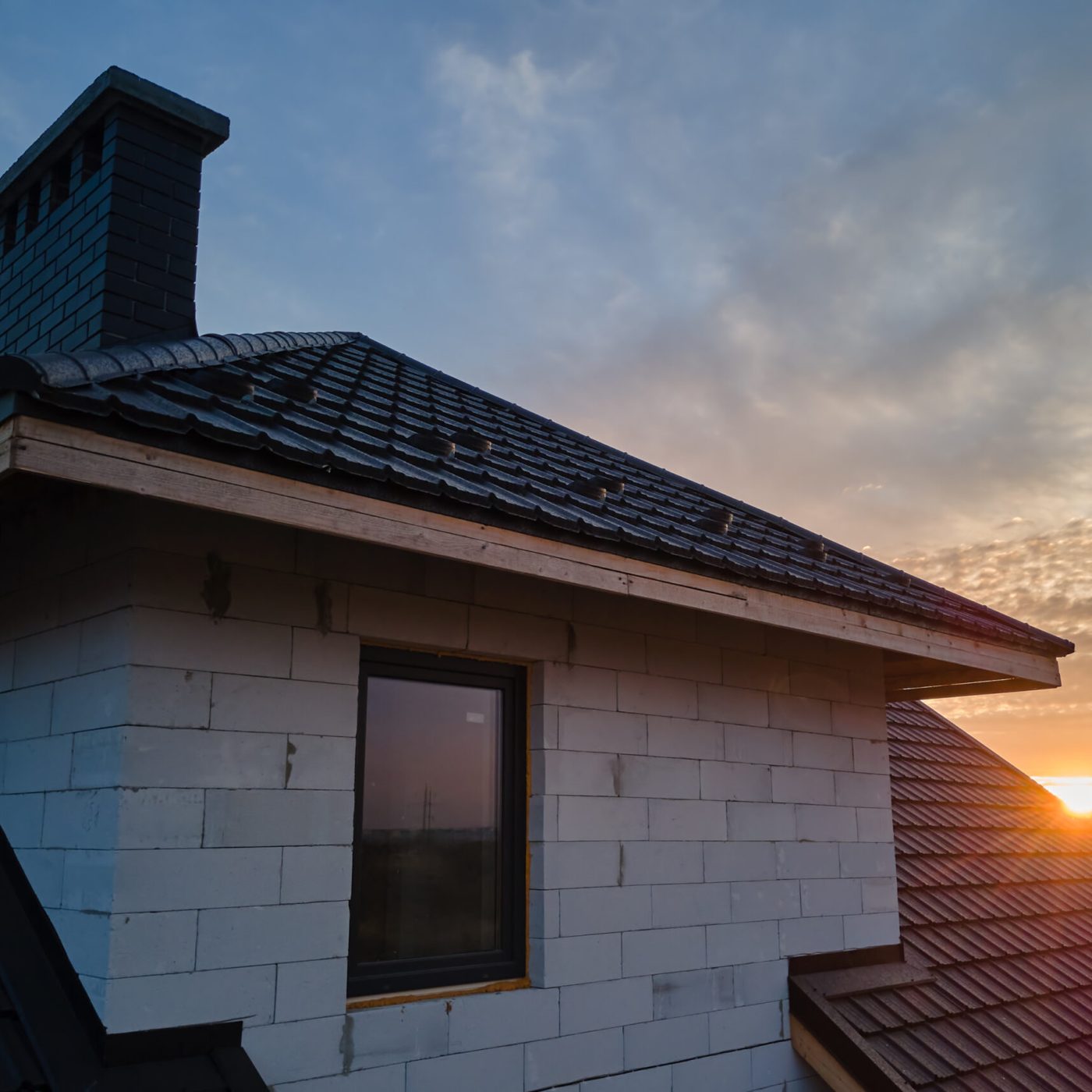 Unfinished house with aerated lightweight concrete walls and wooden roof frame covered with metallic tiles under construction.